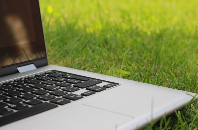Ein aufgeklappter Laptop liegt im Gras.