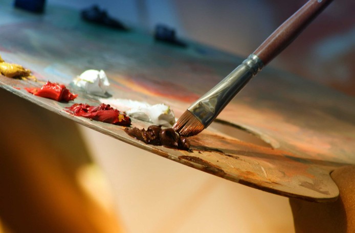 Auf einer Malerpalette sind mehrere Kleckse mit Farbe, und ein Pinsel wird in einen Farbklecks getunkt.