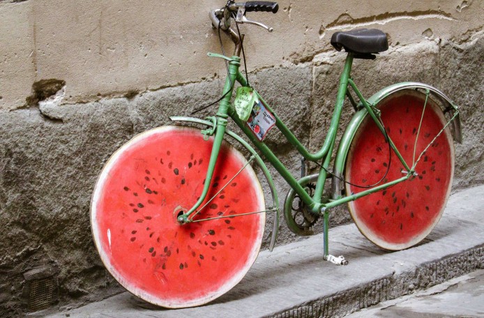 Ein grünes Fahrrad lehnt an einer Wand. Die Räder sehen aus wie eine angeschnittene Wassermelone.