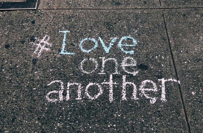 #Love one another steht mit bunter Kreide auf graue Gehwegplatten geschrieben - SCHOKOLADENSEITE.net übernimmt Verantwortung.